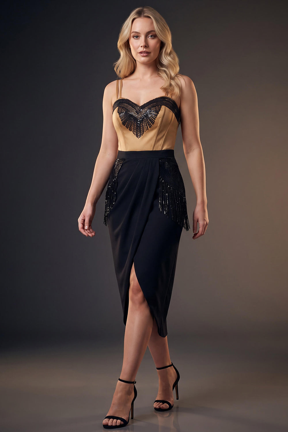 A woman models a Luxe Noir sleeveless evening gown with a beige and black sweetheart bodice, black beaded fringe details, and a black high-slit skirt against a dark gray studio background.