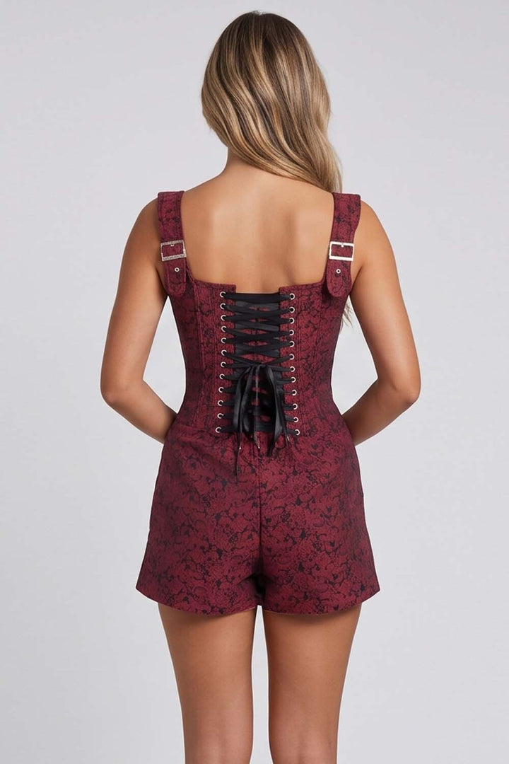 A woman viewed from the back wearing a sleeveless Corset Skort short romper with a dark red and black floral pattern, wide shoulder straps, and a black lace-up back.