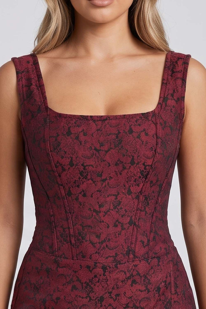 A close-up of a model wearing a sleeveless Corset Skort , square-neck bodysuit or dress in a dark red and black floral jacquard pattern.