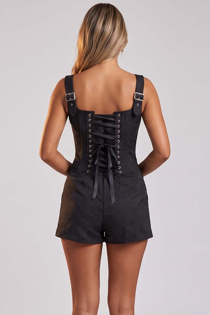 A woman shown from the back wearing a black Luxe Noir Corset Skort   with shoulder straps and metal buckle details, photographed against a light gray studio background.