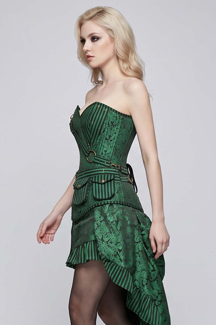 A blonde model wearing a dark green LUXE NOIR CORSET strapless corset-style dress with lace and striped fabric details, paired with sheer black tights, against a light gray studio background.