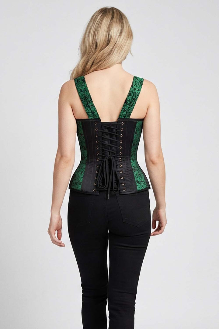 A woman shown from the back wearing a  black corset-style top with green patterned shoulder straps and black lace-up detailing, paired with black pants, against a light gray studio background.