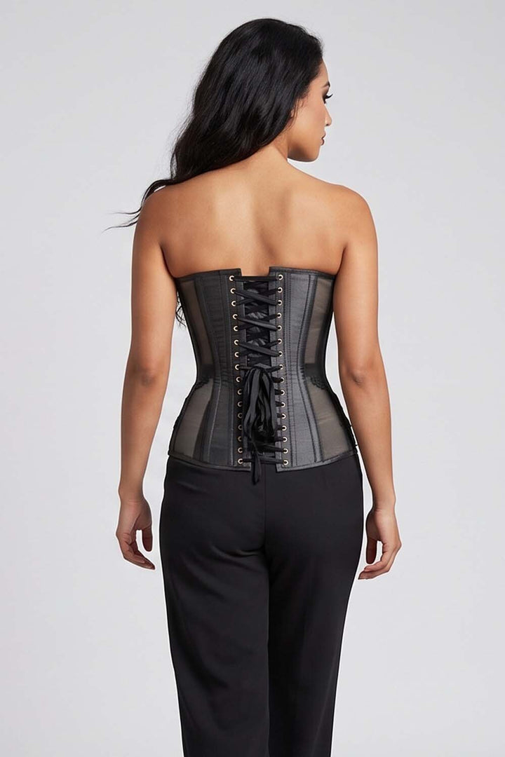 A woman shown from the Luxe Noir  back wearing a strapless black corset-style top with lace-up front and black pants, photographed against a light gray studio background.